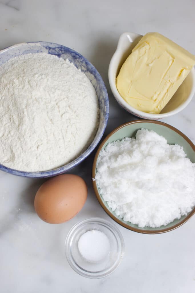 kommetjes met ingredienten voor appeltaartdeeg: bloem, suiker, boter, zout en een ei
