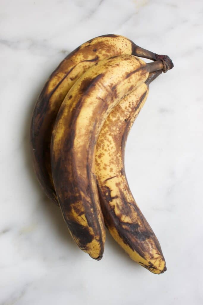 drie hele rijpe bananen waarvan de schil grotendeels al bruin is