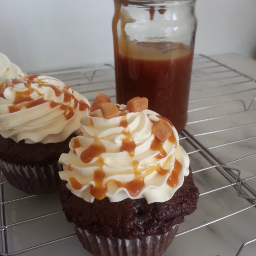 frappuccino cupcakes gedecoreerd met een toef botercrime, karamelsaus en karamel blokjes op een taartrooster. Er achter staat een potje met karamelsaus.