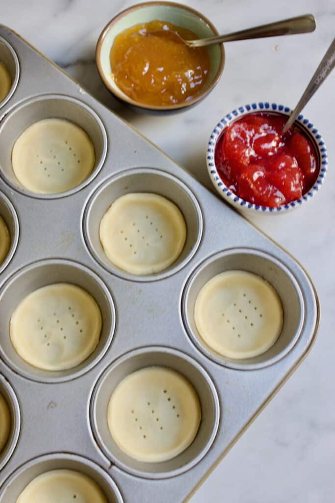 deegrondjes in een muffinvorm met een bakje met jam ernaast.