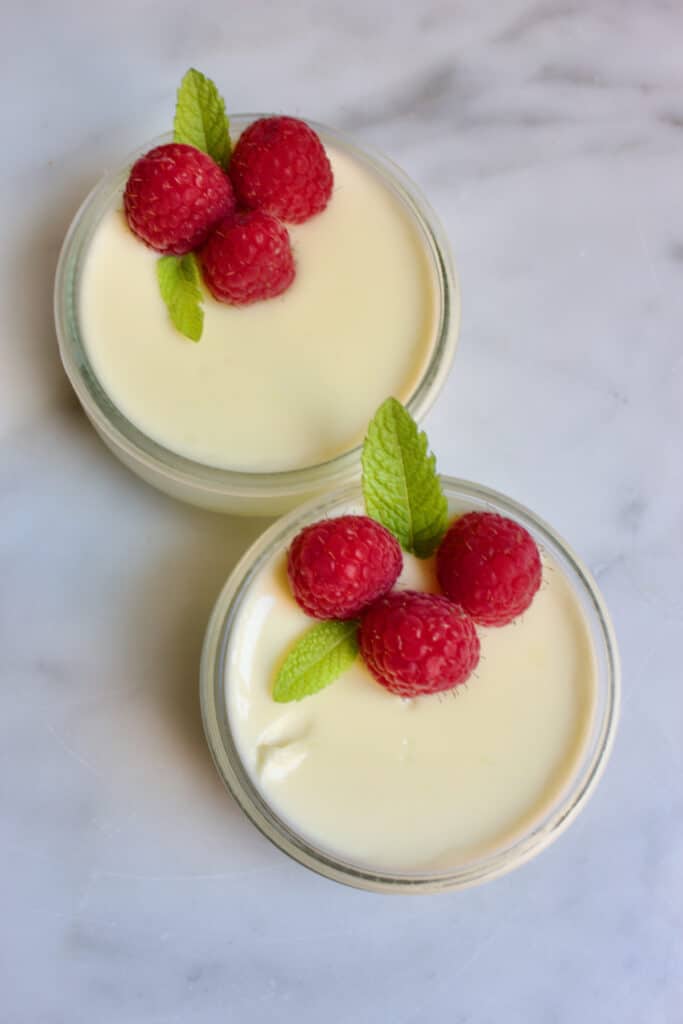 twee schaaltjes met limoencrime (lime posset) van bovenaf gezien. Erop ligt een decoratie van frambozen en muntblaadjes