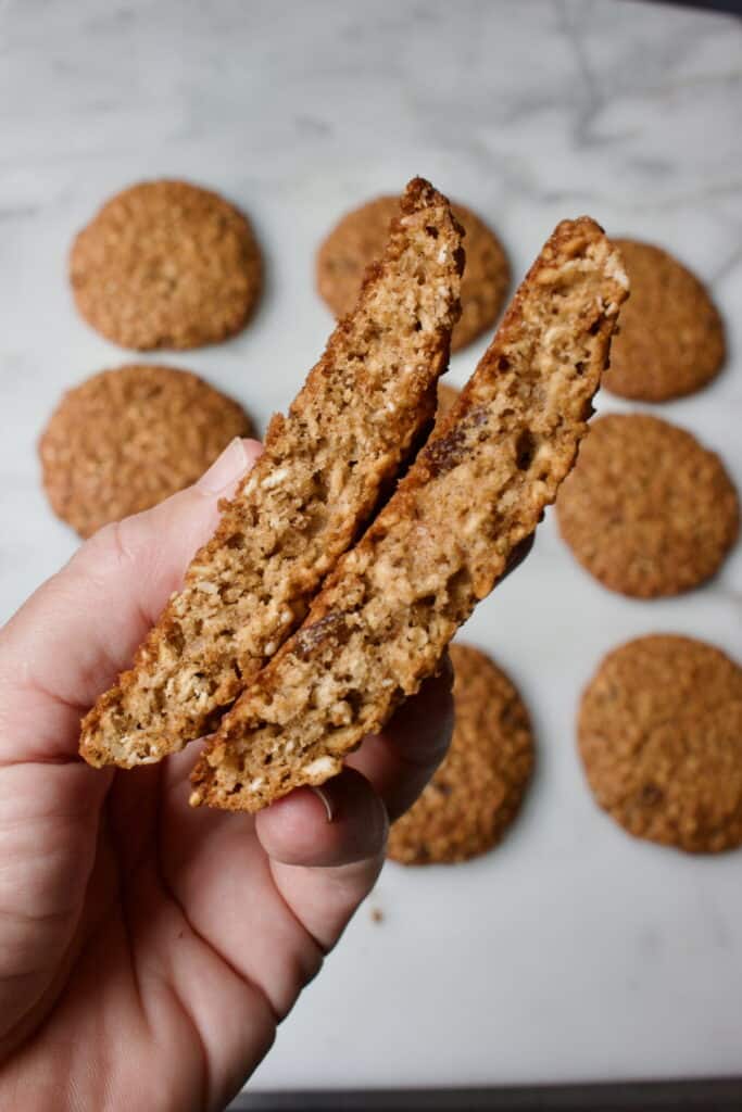 een doormidden gebroken havermout koek met op de achtergrond acht hele koeken.