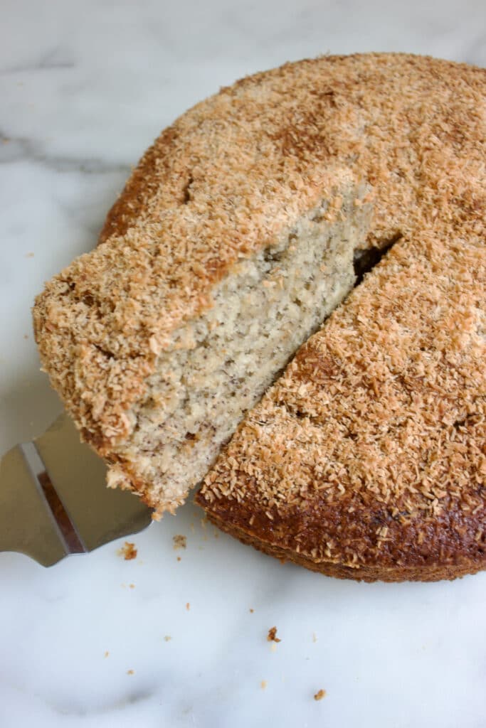 een ronde kokos banananecake waaruit een punt cake gehaald wordt met een taartschep