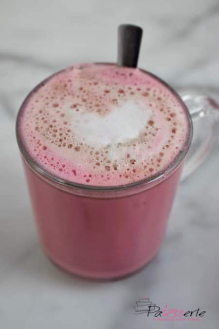 Een mok met Red Velvet Latte. Koffie met roze melk en een klein laagje melkschuim. Gemaakt met bietensap voor de roze kleur en chocolade voor de red velvet smaak