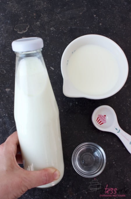 fles zelf gemaakte karnemelk met een kom melk, maatschep en glazen schaaltje met azijn