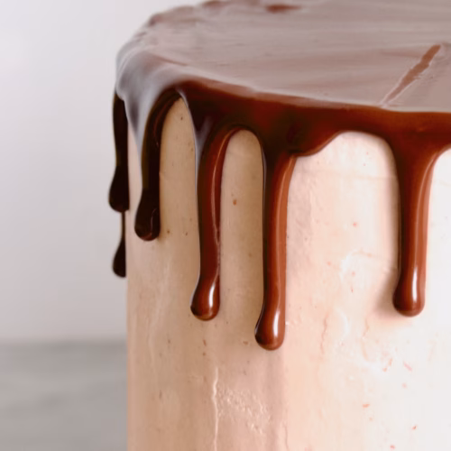 zijkant van een roze taart waar een chocolade drip op zit