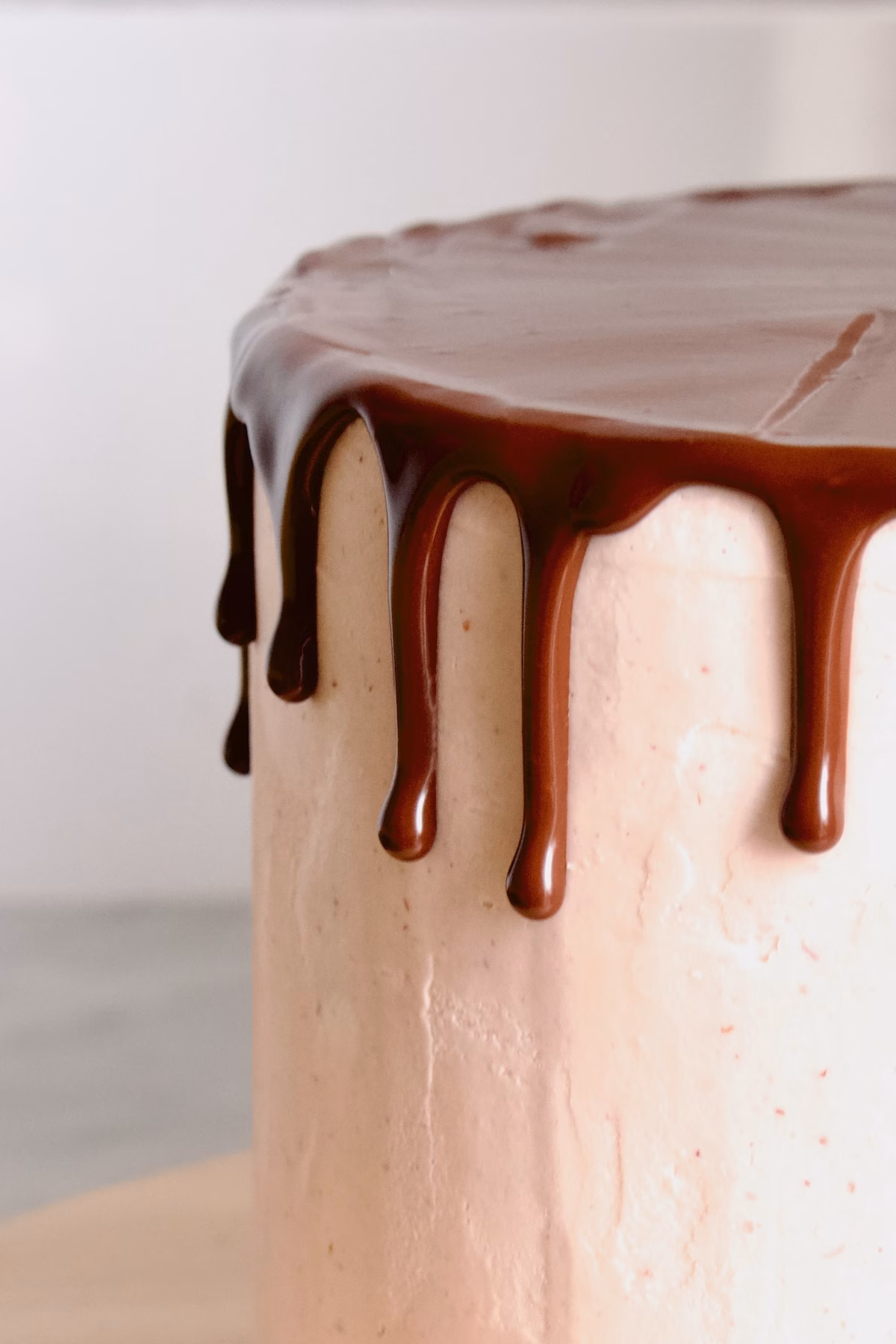 zijkant van een roze taart waar een chocolade drip op zit
