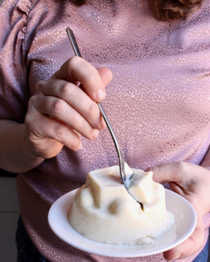 Vanille pudding op een schotel waar met een lepel een hap uitgenomen wordt