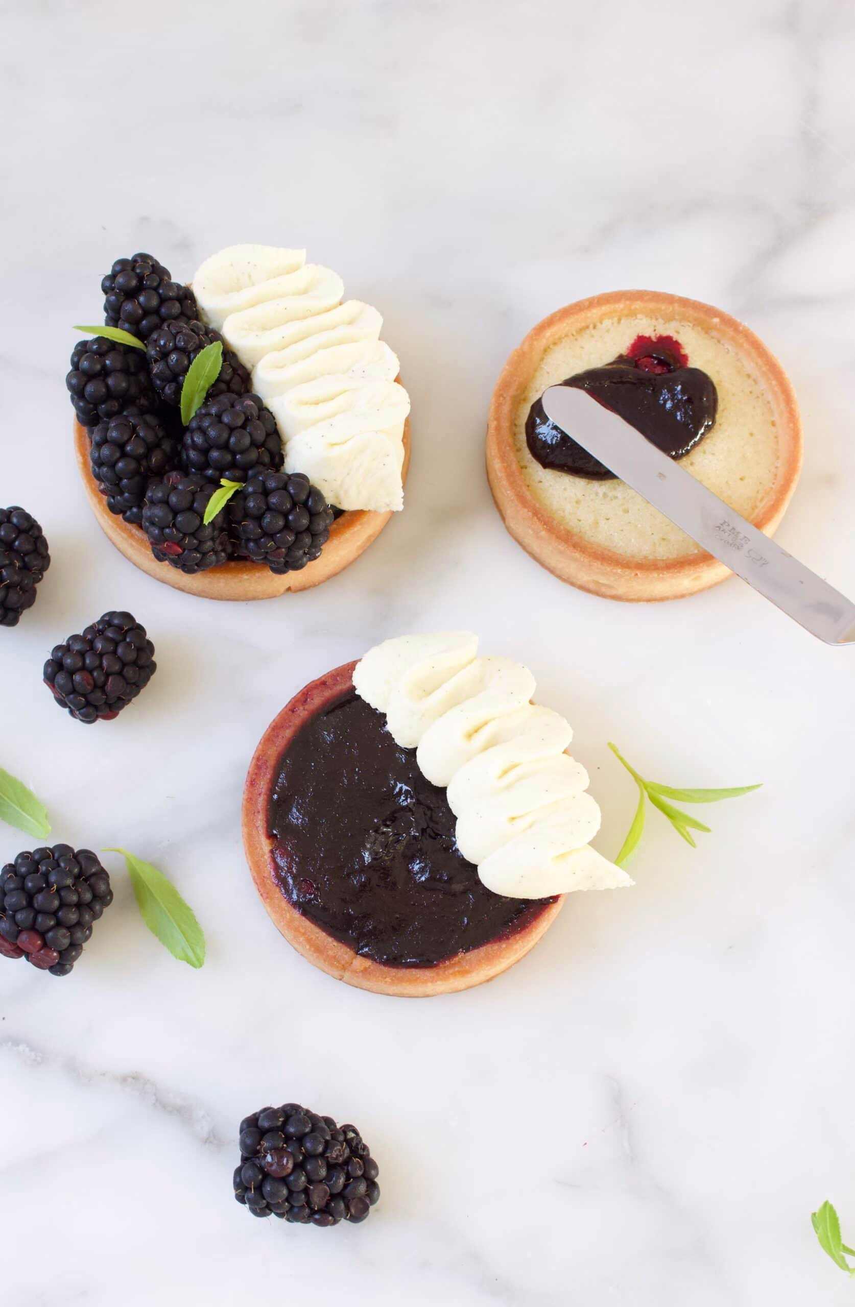 twee tartelettes met bramen en slagroom, de derde tartelette wordt gevuld met bramenjam