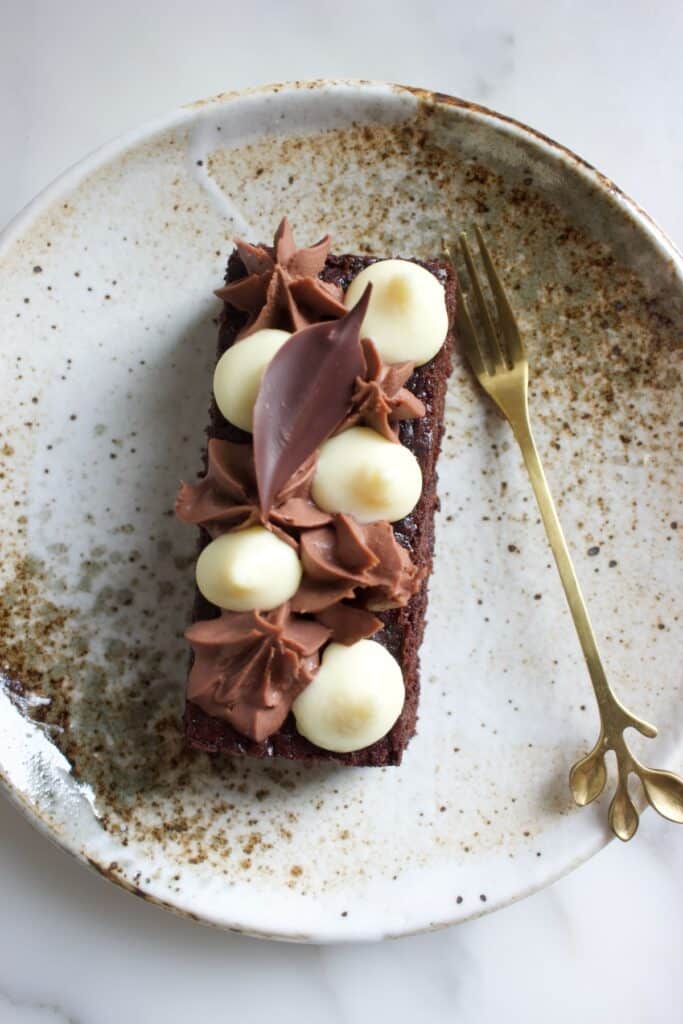 chocoladecake met cacaojuice ganache decoratie op een taartschotel en een goudkleurig vorkje ernaast