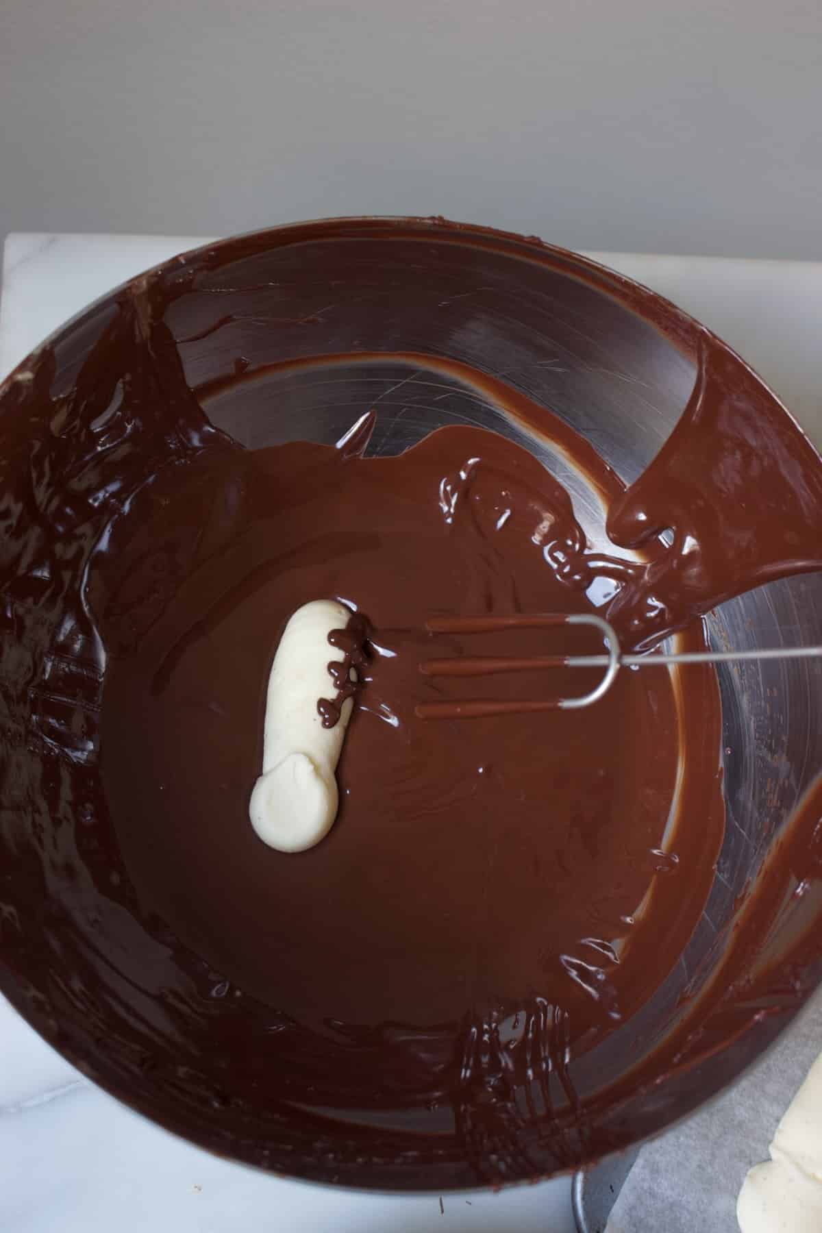 een bevroren vulling van een slagroomtruffel in een kom met chocolade, waarbij een bonbonvorkje wordt gebruikt om de vulling in de chocolade te dompelen