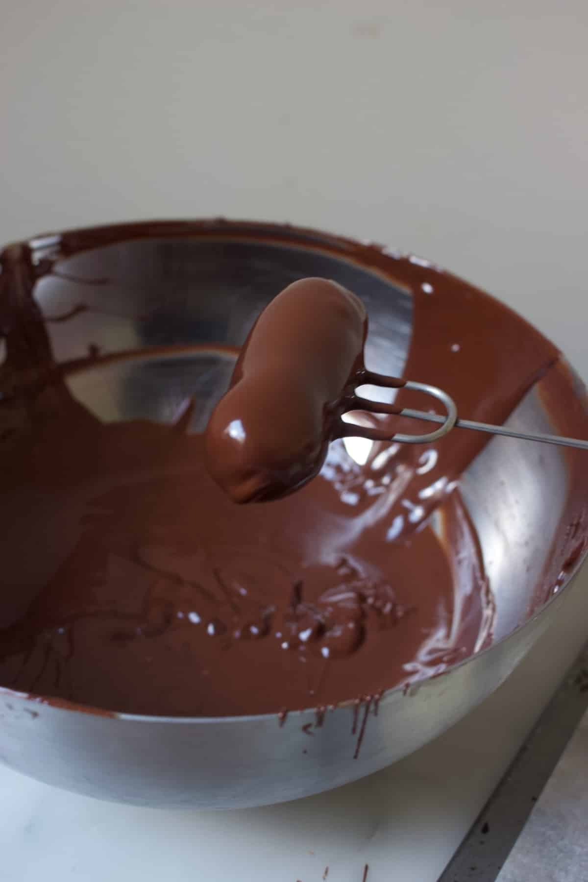 een slagroomtruffel die net door de gesmolten chocolade is gehaald en nu op een bonbonvorkje ligt