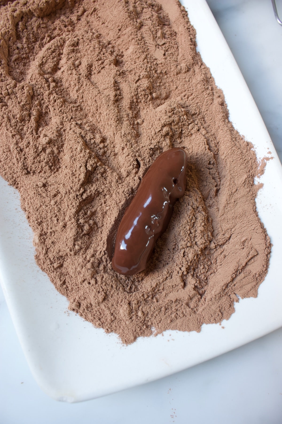 een slagroomtruffel op een rechthoekig bord met cacaopoeder