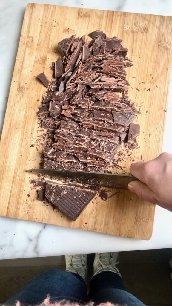 Een blok chocolade fijnhakken met een mes op een houten snijplank