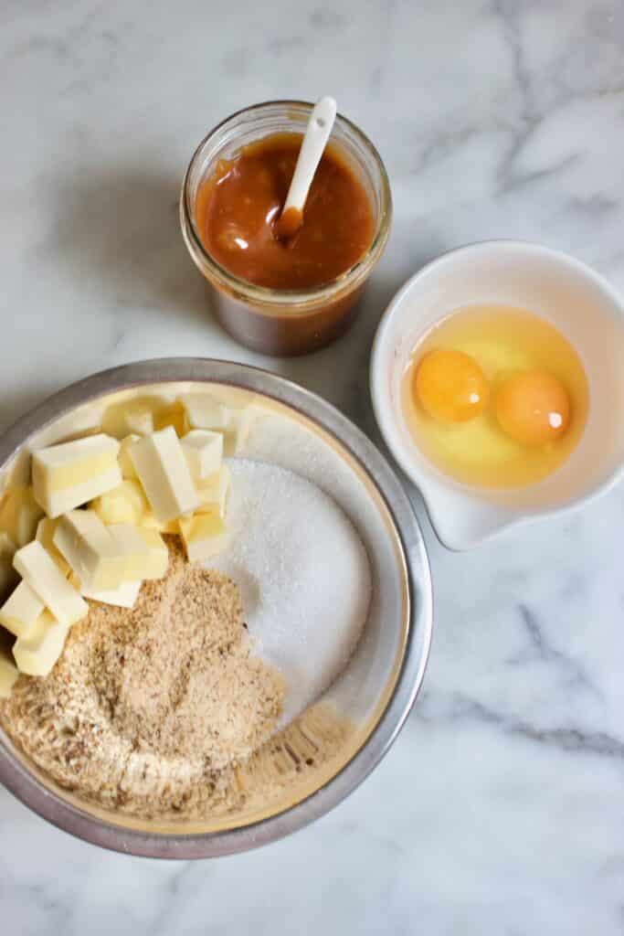 ingredienten voor de vulling van een drie koningen taart: hazelnootmeel, boter en suiker, twee eieren en een potje met karamlel