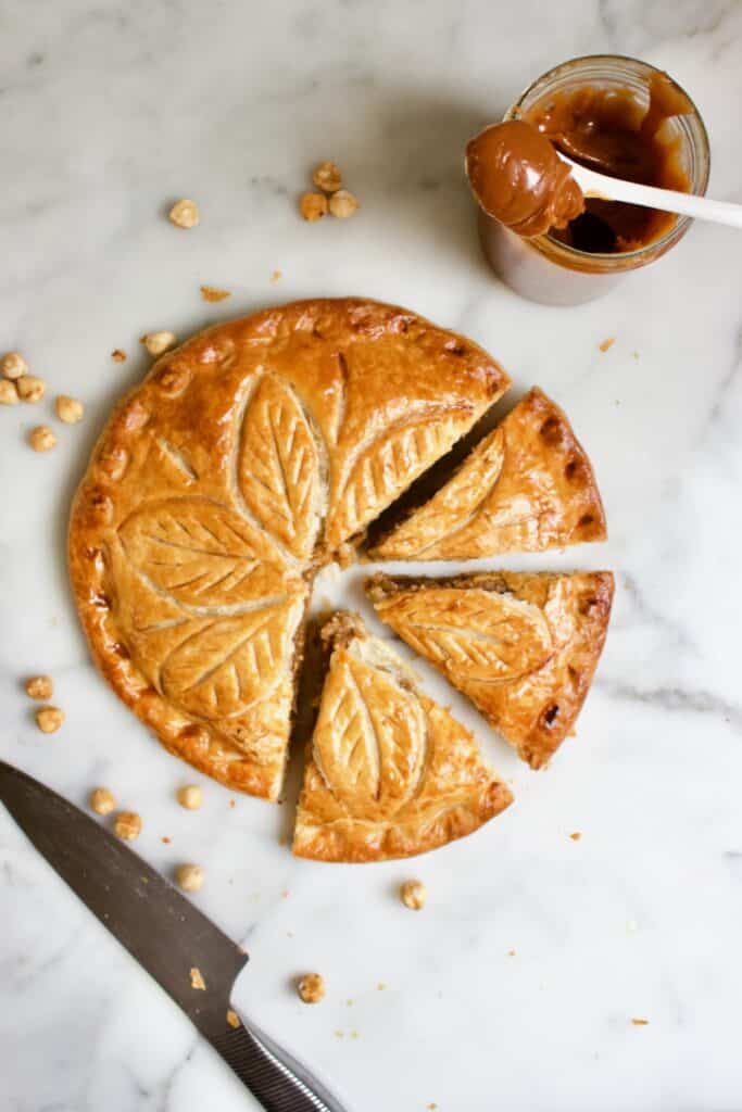 drie koningen taart met hazelnoot en karamel, waar drie punten uit gesneden zijn en er een pot met karamel naast staat 