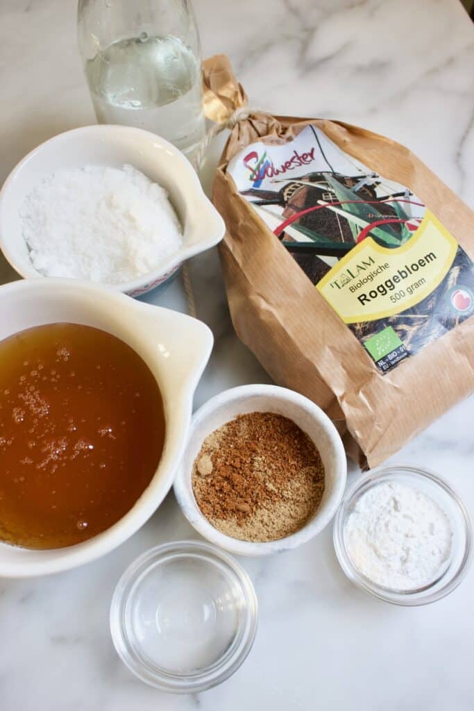 ingredienten voor het maken van friese keallepoat koek: een zak roggebloem, kommetjes met suiker, specerijen en honing