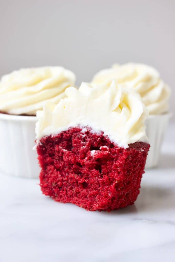 drie red velvet cupcakes met een witte toef roomkaas creme. de voorste cupcake is uit het cupcake papiertje gehaald.