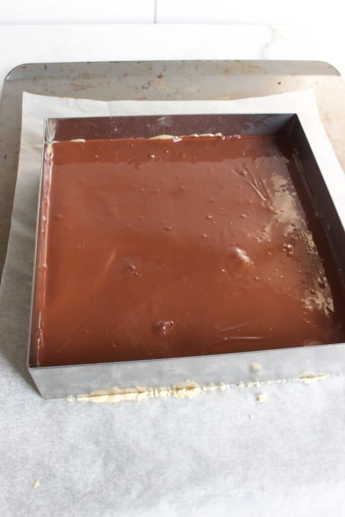 vierkante bakvorm met chocolade op een karamel en koeklaag