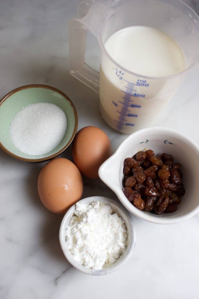 ingredienten om vanille pudding met boerenjongens te maken: schaaltjes met suiker, maizena, boerenjongens, melk en twee losse eieren