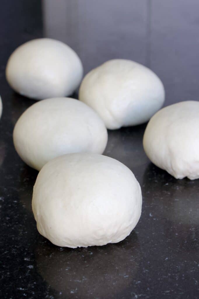 vijf bolletjes witbrood deeg die opgebold zijn voor kleine broodjes.