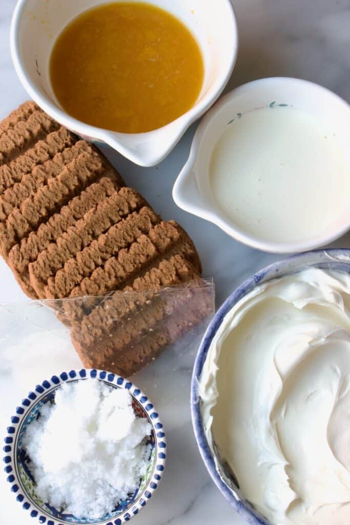 ingredienten voor cheesecake in een glas met passievrucht: schaaltjes met passievrucht puree, slagroom, suiker en roomkaas. Daarnaast liggen bastogne koekjes en blaadjes gelatine.