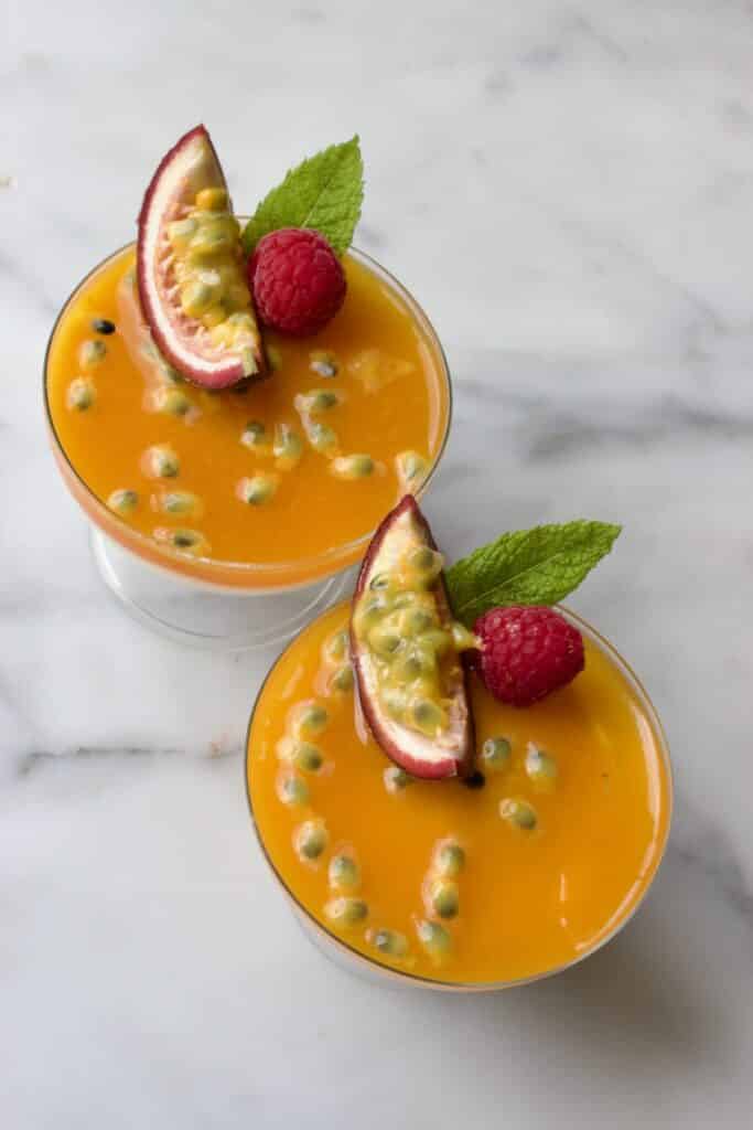 twee glaasjes met cheesecake met passievrucht toetjes gedecoreerd met passievrucht, munt en framboos