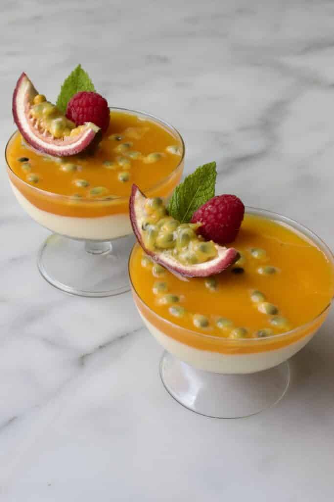 twee glaasjes met cheesecake met passievrucht toetjes gedecoreerd met passievrucht, munt en framboos