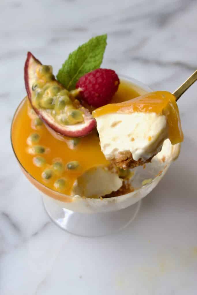 cheesecake in een glas met passievrucht waarbij er met een lepel een hapje uitgehaald wordt