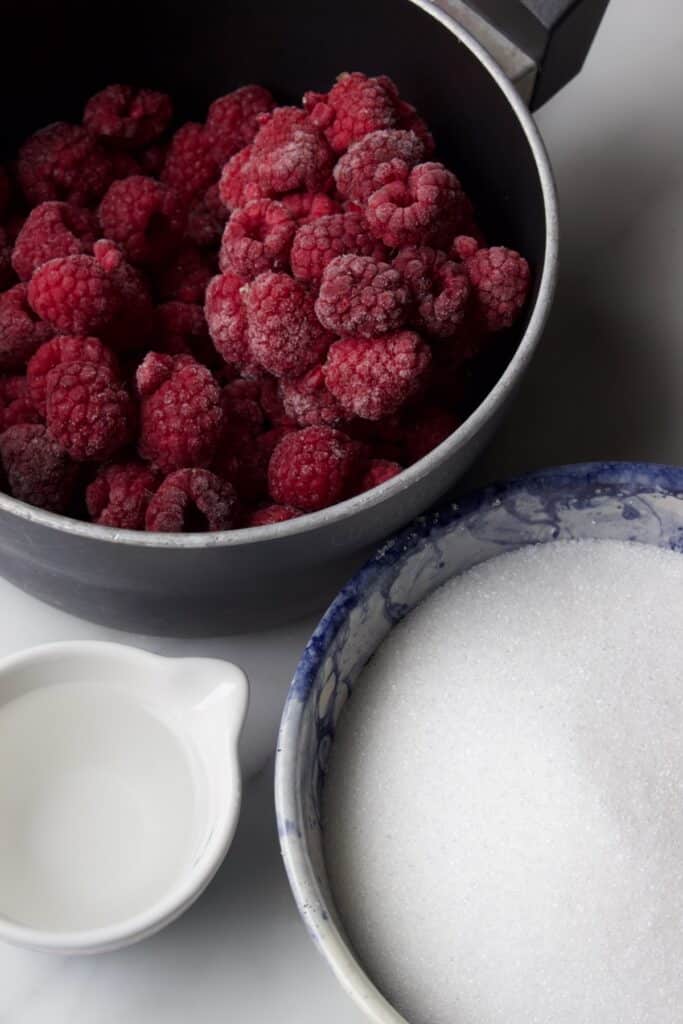 Ingredienten voor frambozensaus (coulis): Diepvries frambozen in een pan, suiker en een beetje water.