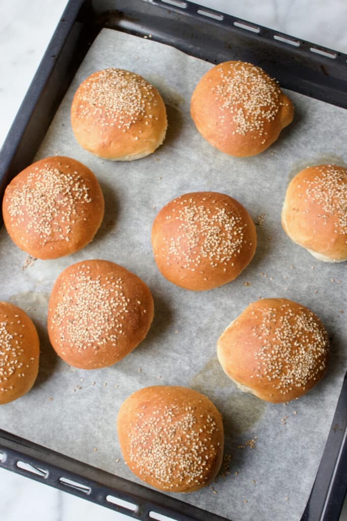 een bakplaat met 9 net gebakken hamburgerbroodjes.