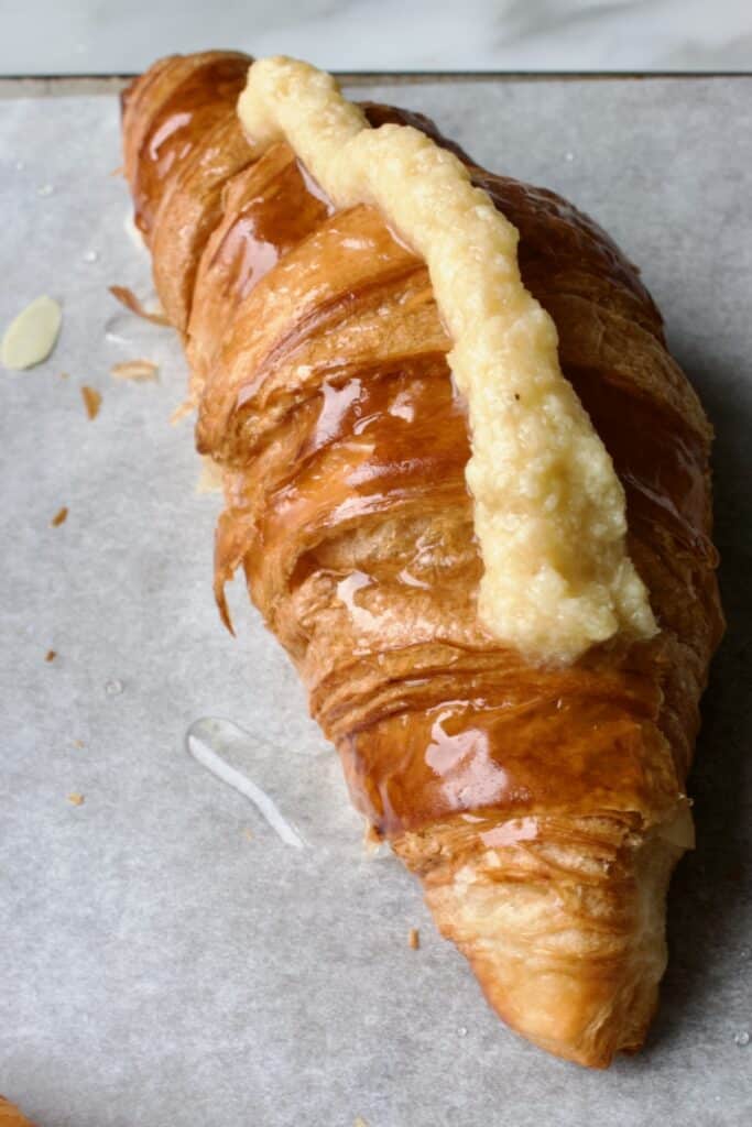 croissant met suikersiroop erop en wat amandelcreme er bovenop waar de geschaafde amandelen op vastgeplakt kunnen worden.