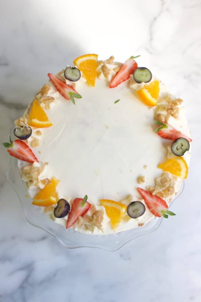 bovenkant van een carrot cake taart welke gedecoreerd is met roomkaas creme en rondom met verse aardbeien, blauwe bessen, walnoot en sinaasappel stukjes