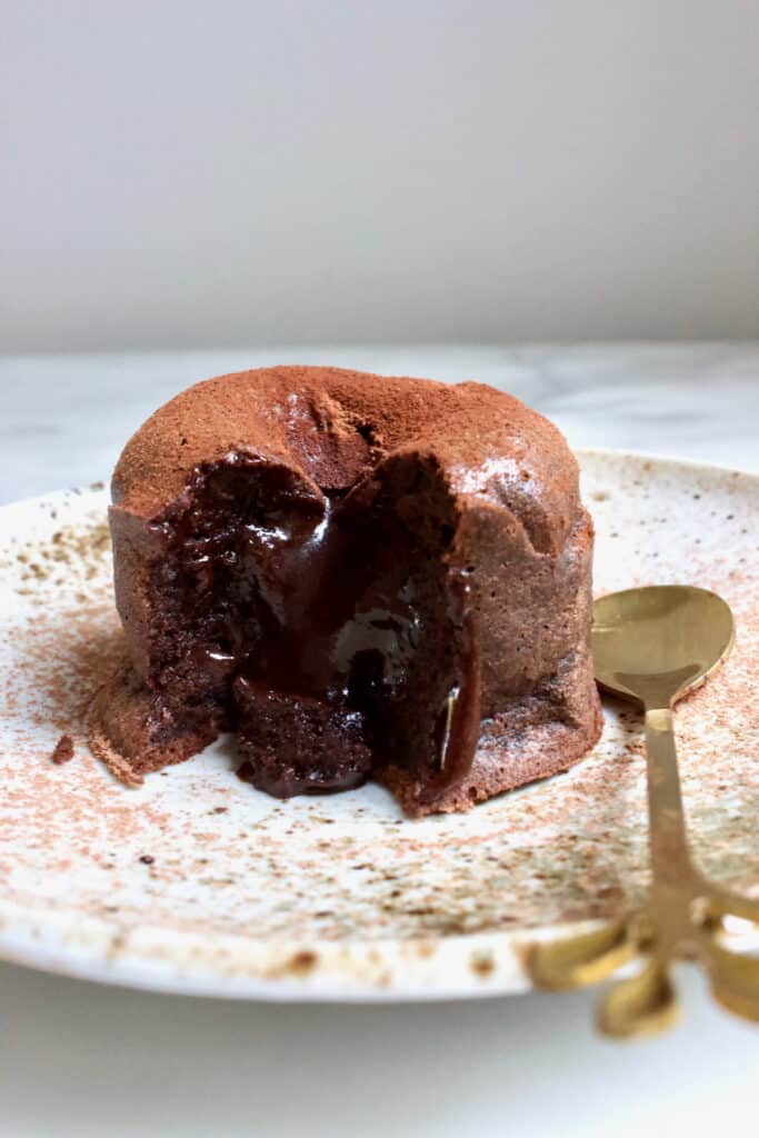 Moelleux op een bord met een gouden lepeltje ernaast, waarbij de vloeibare binnenkant van de lava cake zichtbaar is