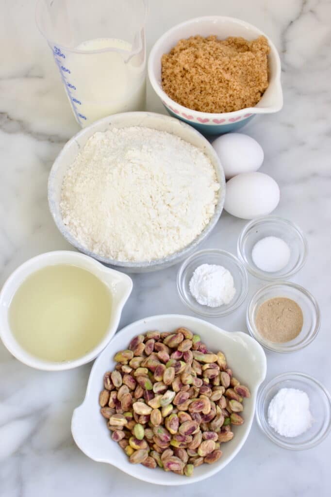 Ingrediënten voor pistache cake in verschillende schaaltjes: karnemelk, basterdsuiker, bloem, eieren, bakpoeder, bakingsoda, zout, kardemom, olie en pistachenoten