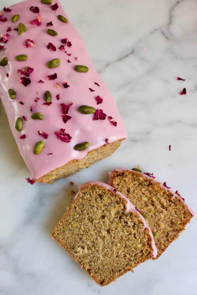 bovenaanzicht van de pistache cake met roos glazuur en twee afgesneden plakjes ervoor