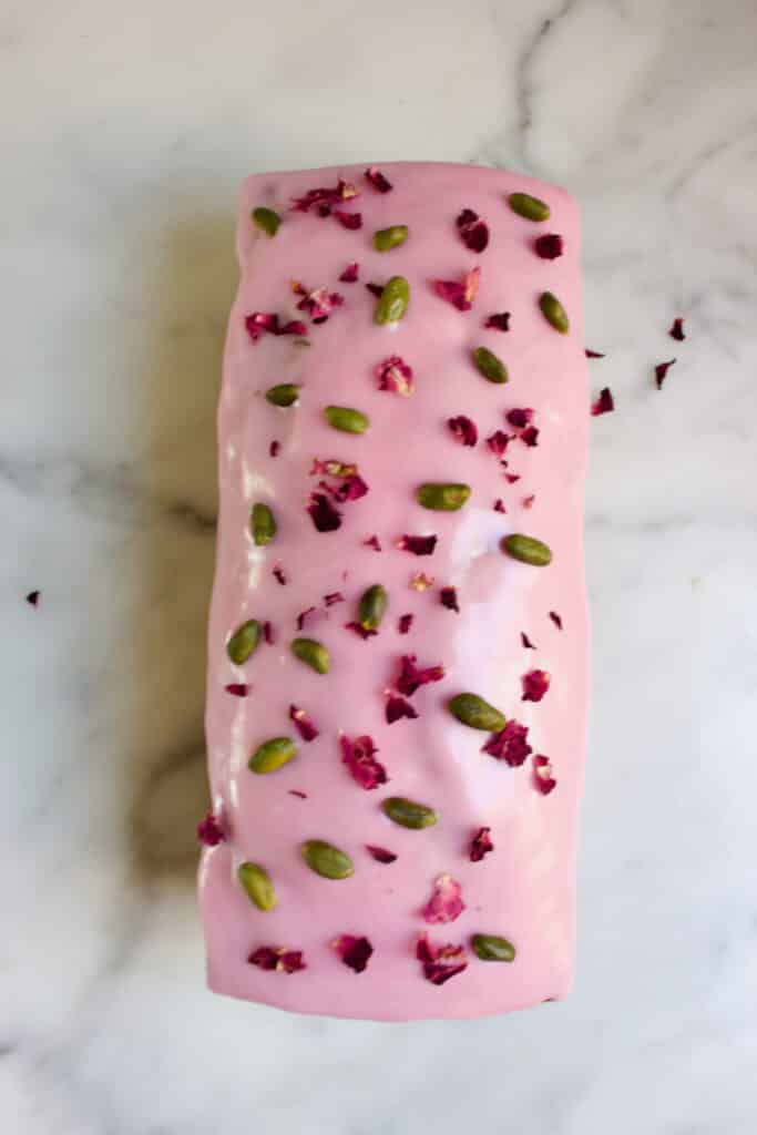 bovenaanzicht van de pistache cake met roos glazuur, rozenblaadjes en groene pistache nootjes