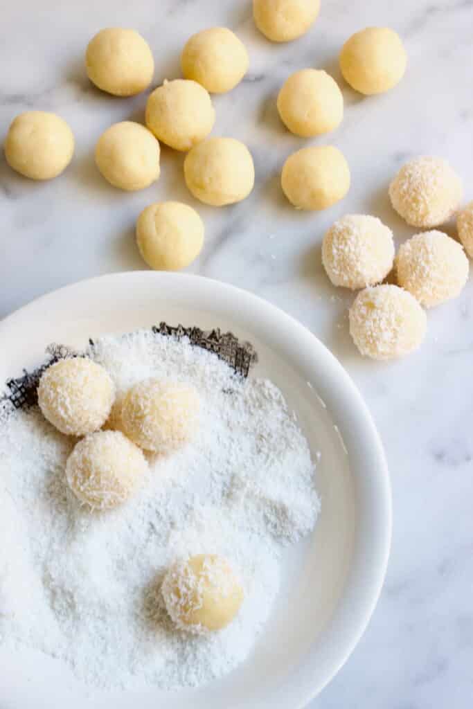 witte brigadeiros rollen door een bord gevuld met kokos
