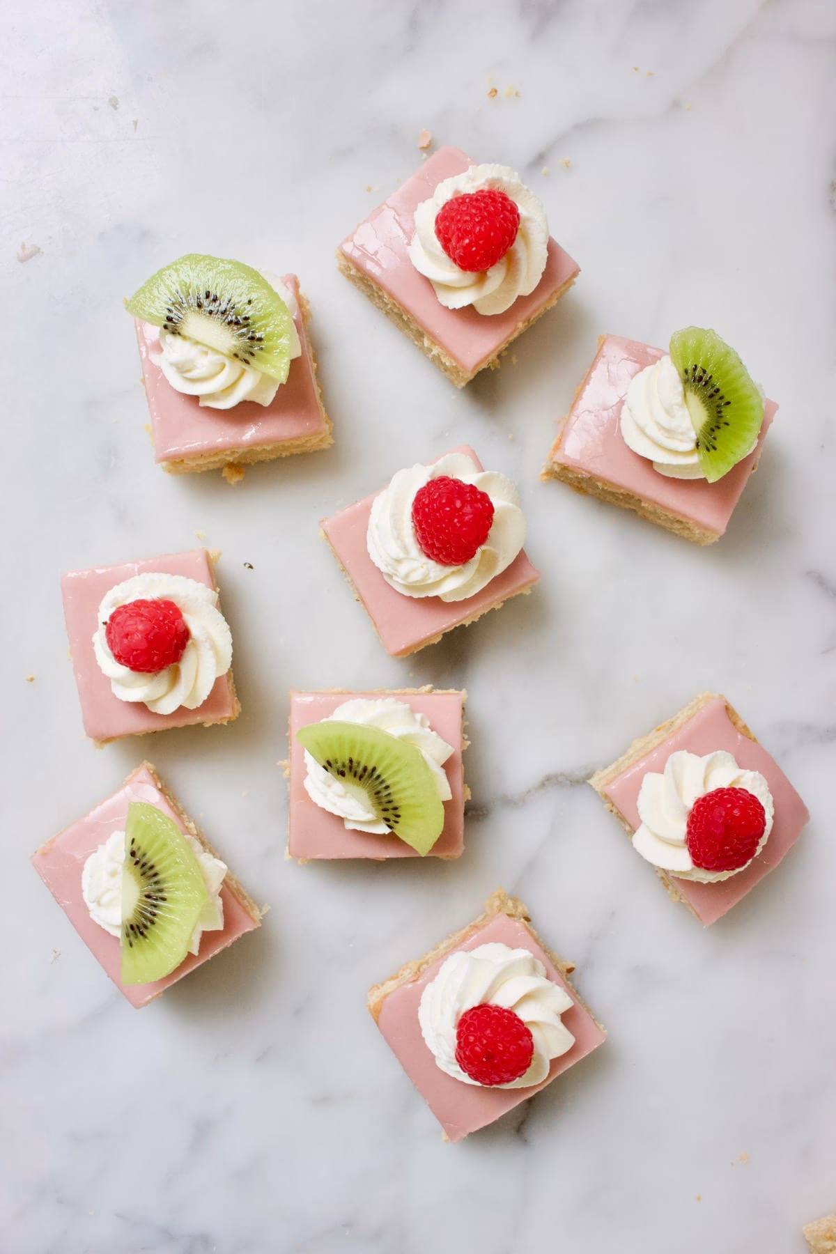 stukjes traditionele Friese oranjekoek. Vierkant, met roze glazuur en gedecoreerd met slagroom en een framboos of stukje kiwi.